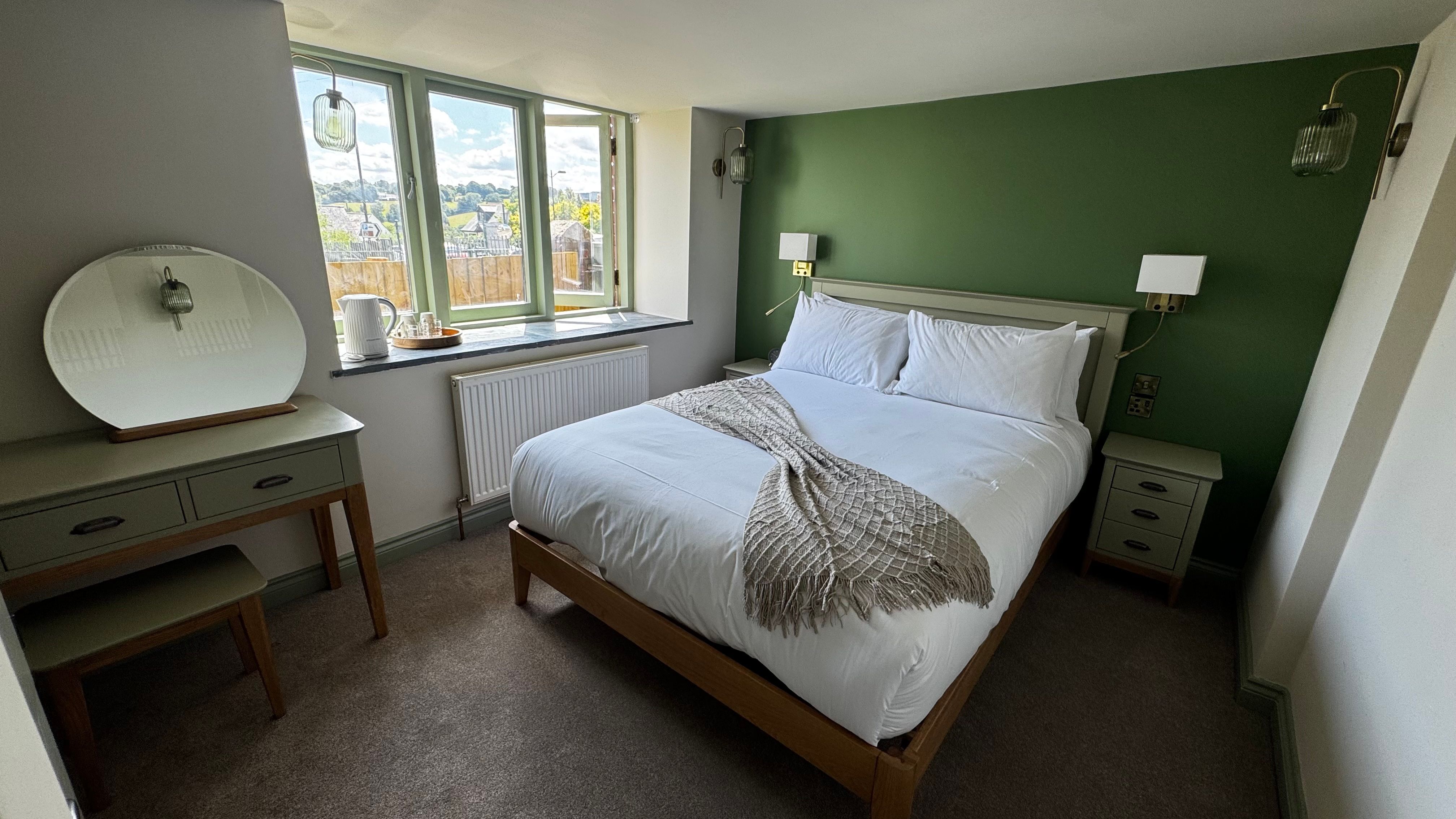 Cozy bedroom with green accent wall, white bedding, and wooden furniture.