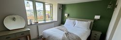 Cozy bedroom with green accent wall, white bedding, and wooden furniture.