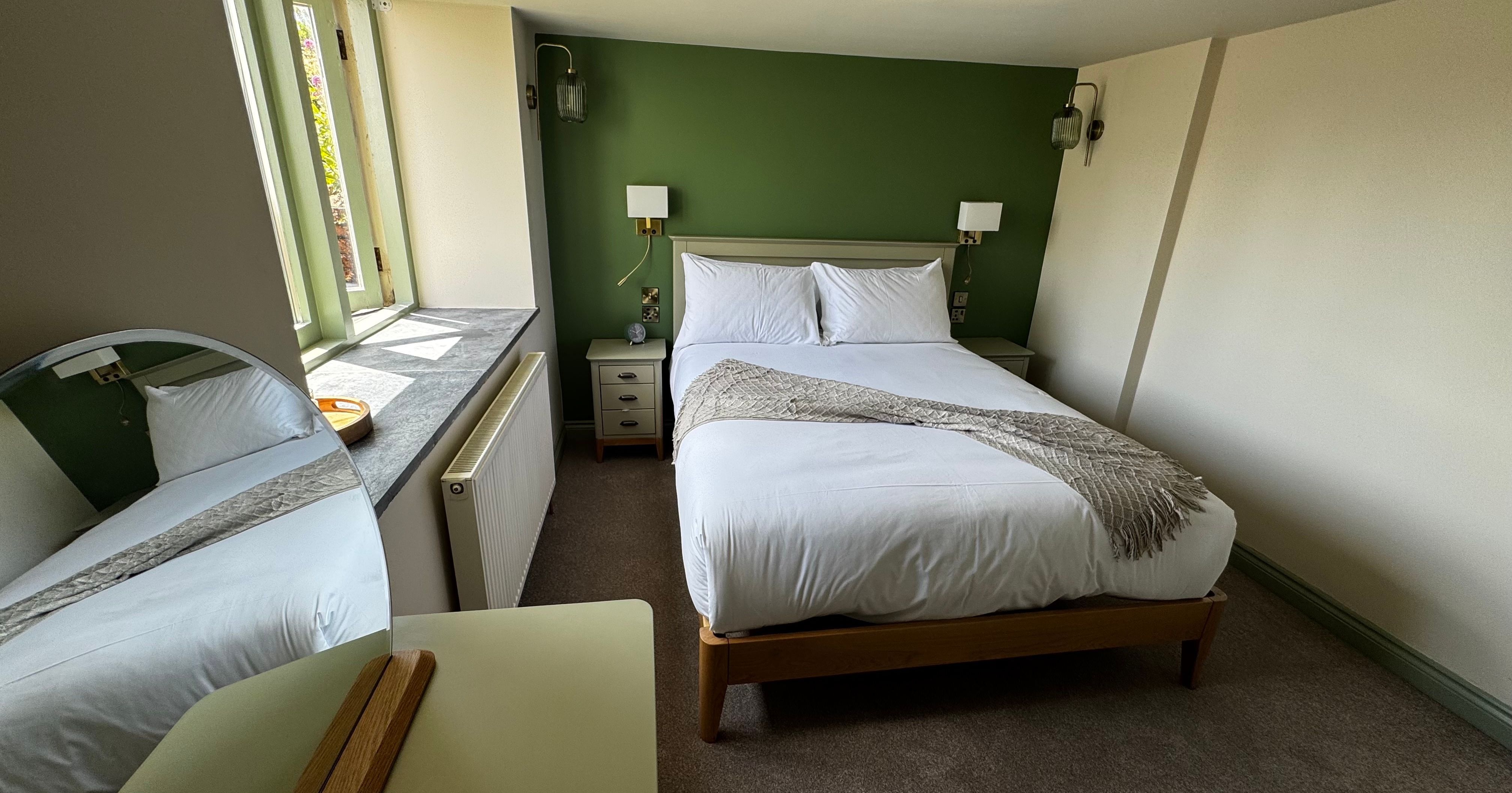 A cozy bedroom with a double bed, green accent wall, and white linens.