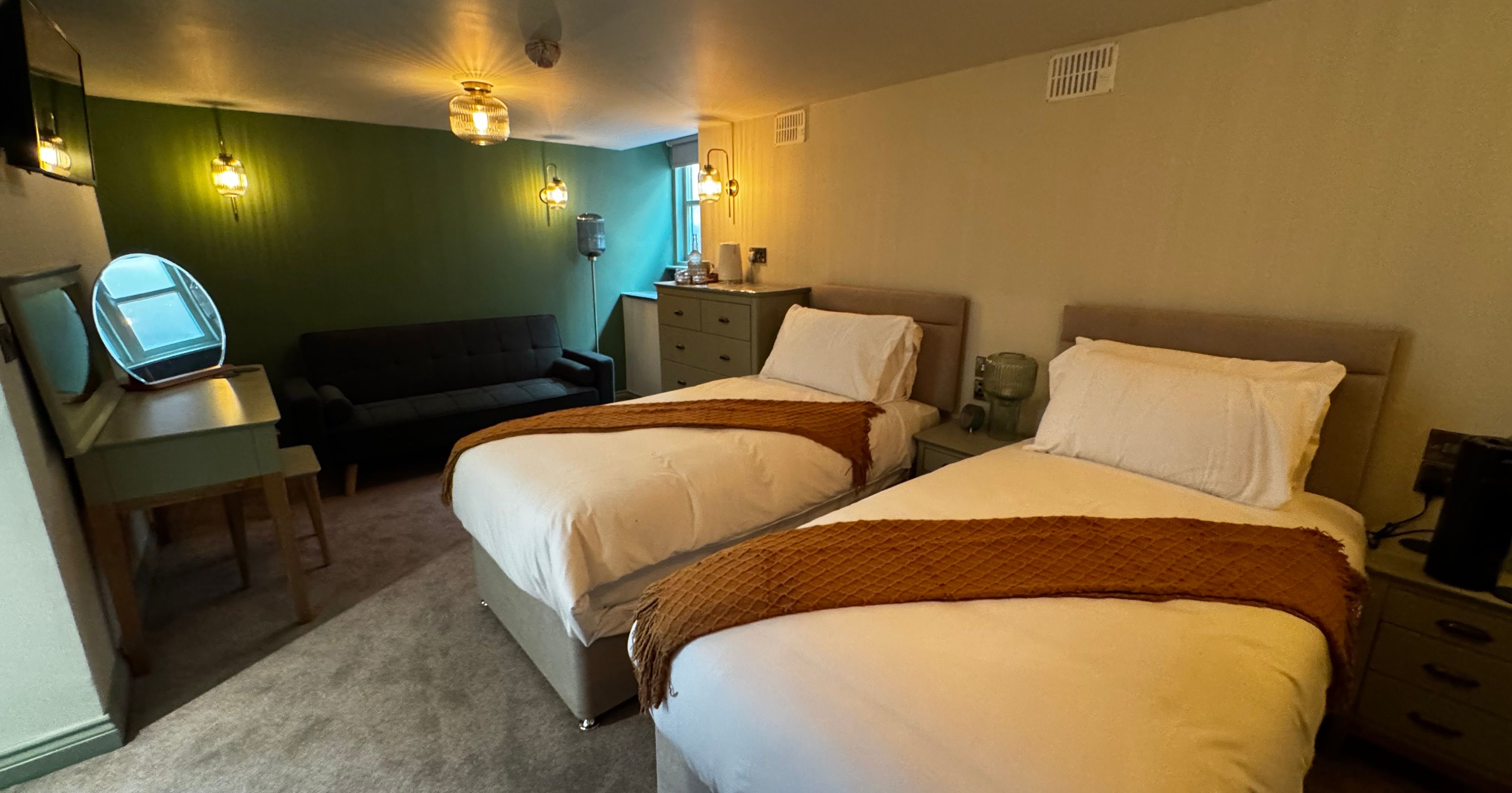 Cozy hotel room with two single beds, sofa, vanity table, and dresser