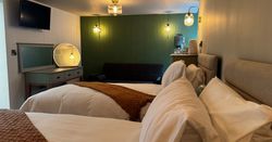 Modern hotel room with two single beds, a green accent wall, and cozy lighting.