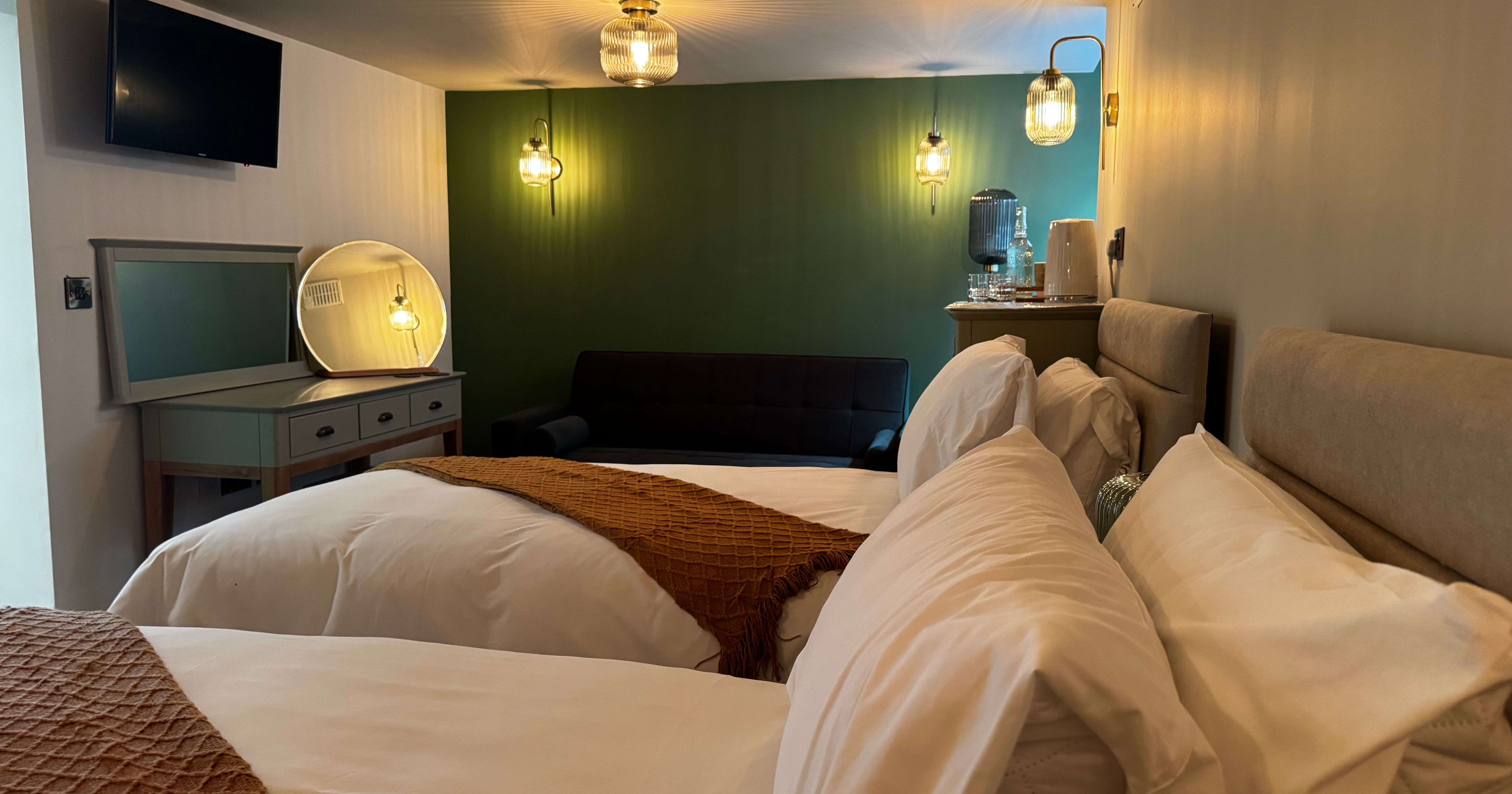 Modern hotel room with two single beds, a green accent wall, and cozy lighting.