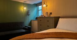 Cozy modern bedroom with green wall, black sofa, chest of drawers, and warm lighting