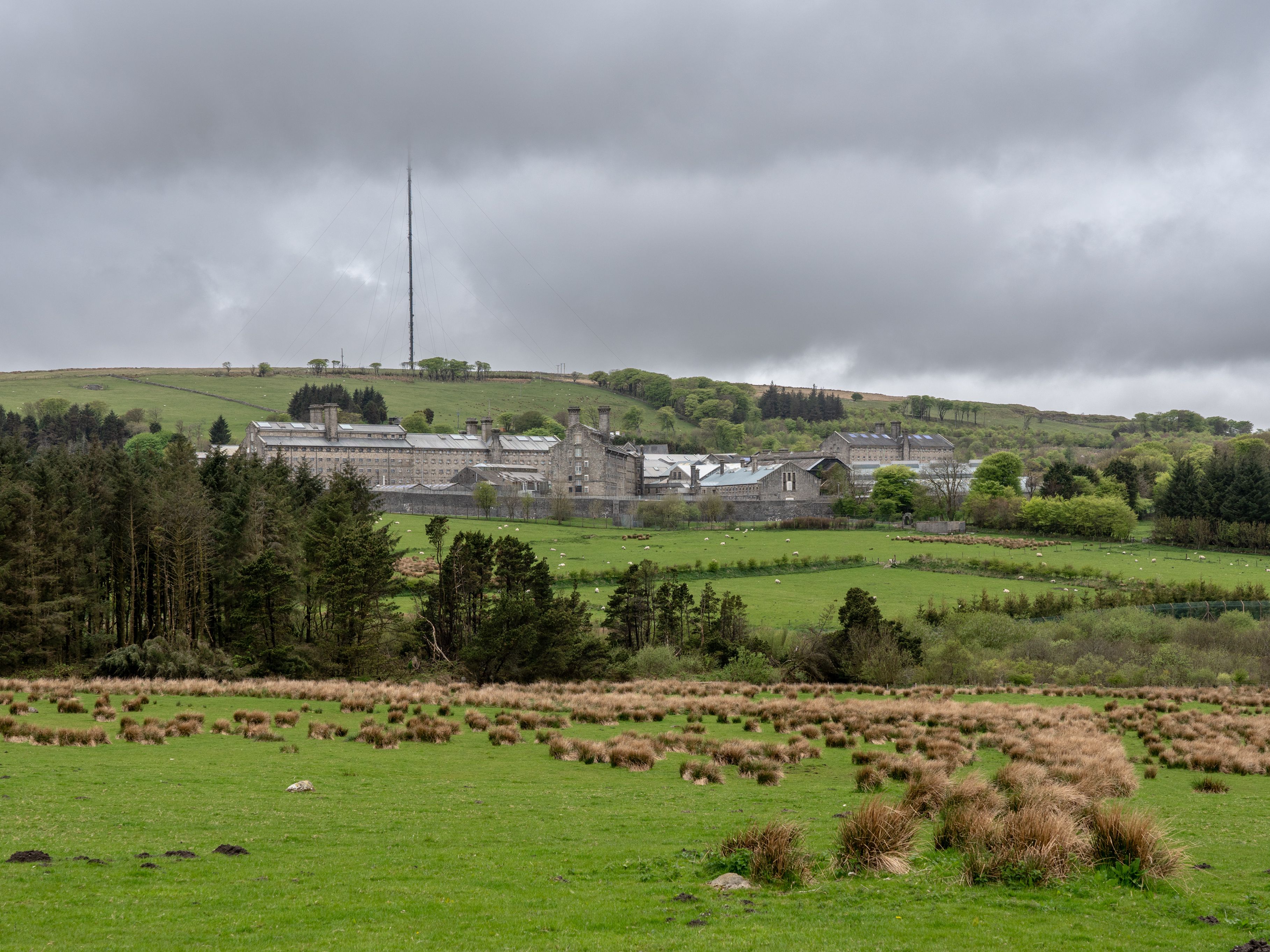 A large stone building complex surrounded by green fields and trees under a cloudy sky.