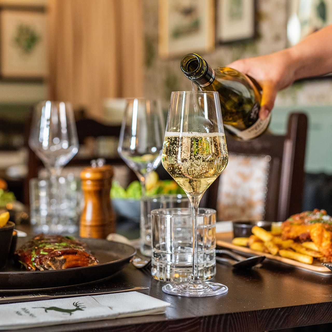 Food on table in restaurant, person pouring glass of wine