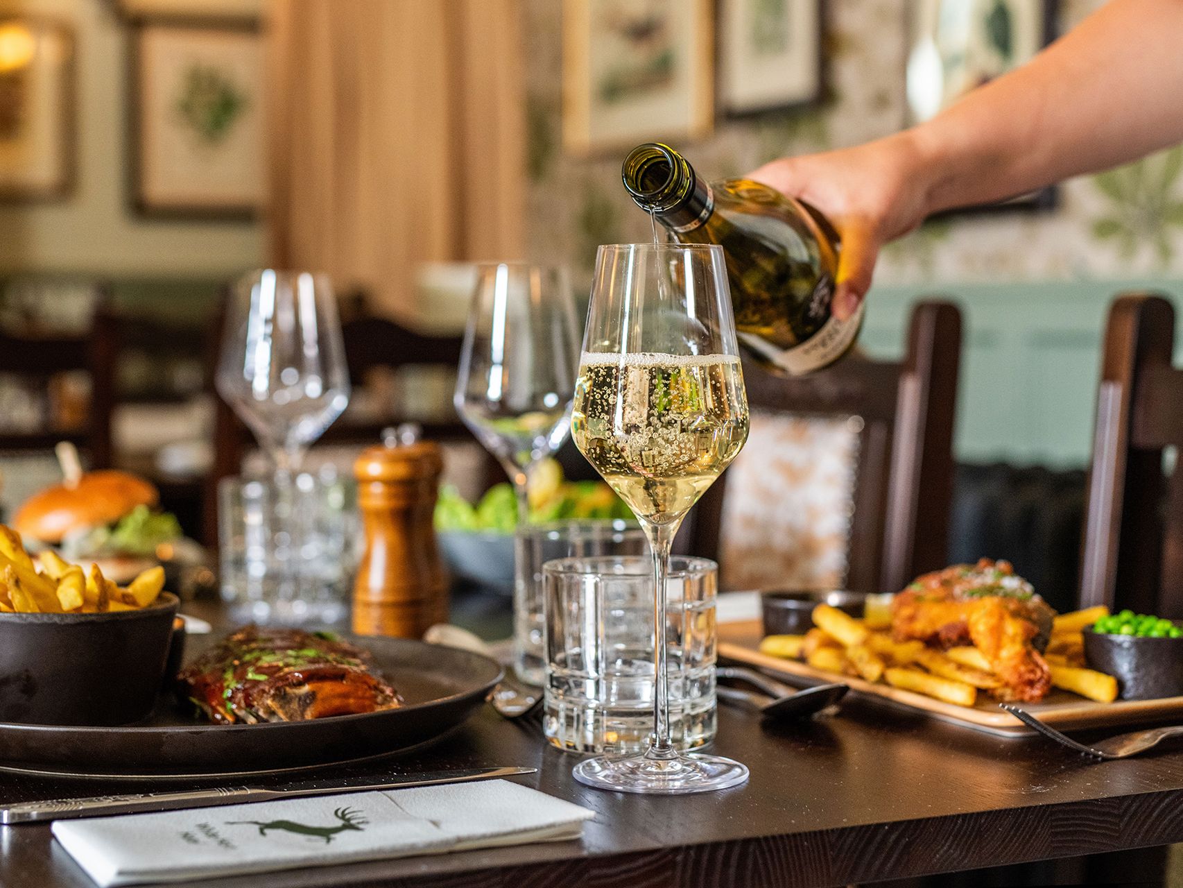 Food on table in restaurant, person pouring glass of wine