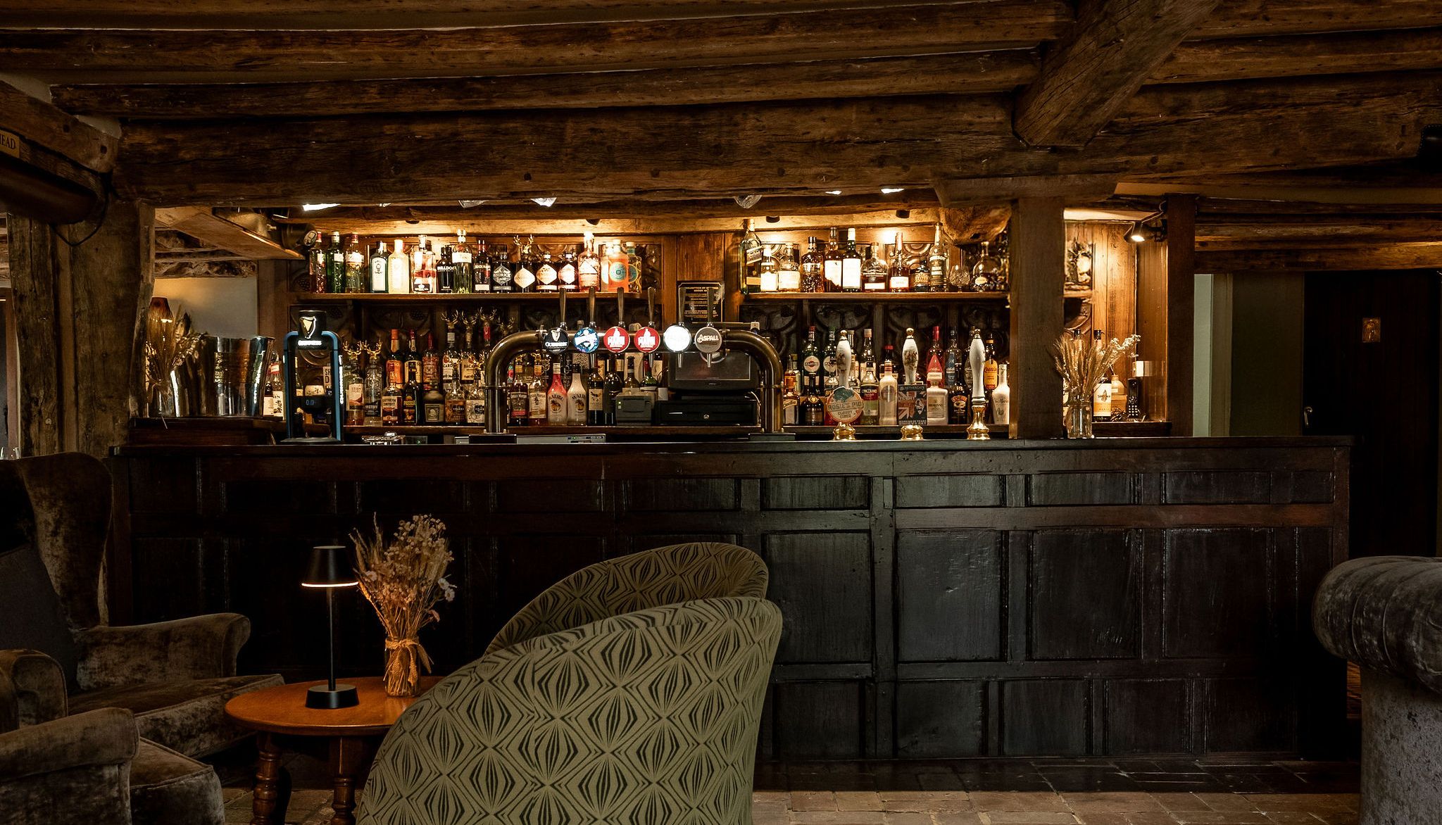 Rustic bar area with wooden beams, cozy armchairs, and a well-stocked bar