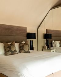 A modern hotel room with a large bed, decorative pillows, nightstands with black lamps, mirrored closet doors, and a wall-mounted TV.