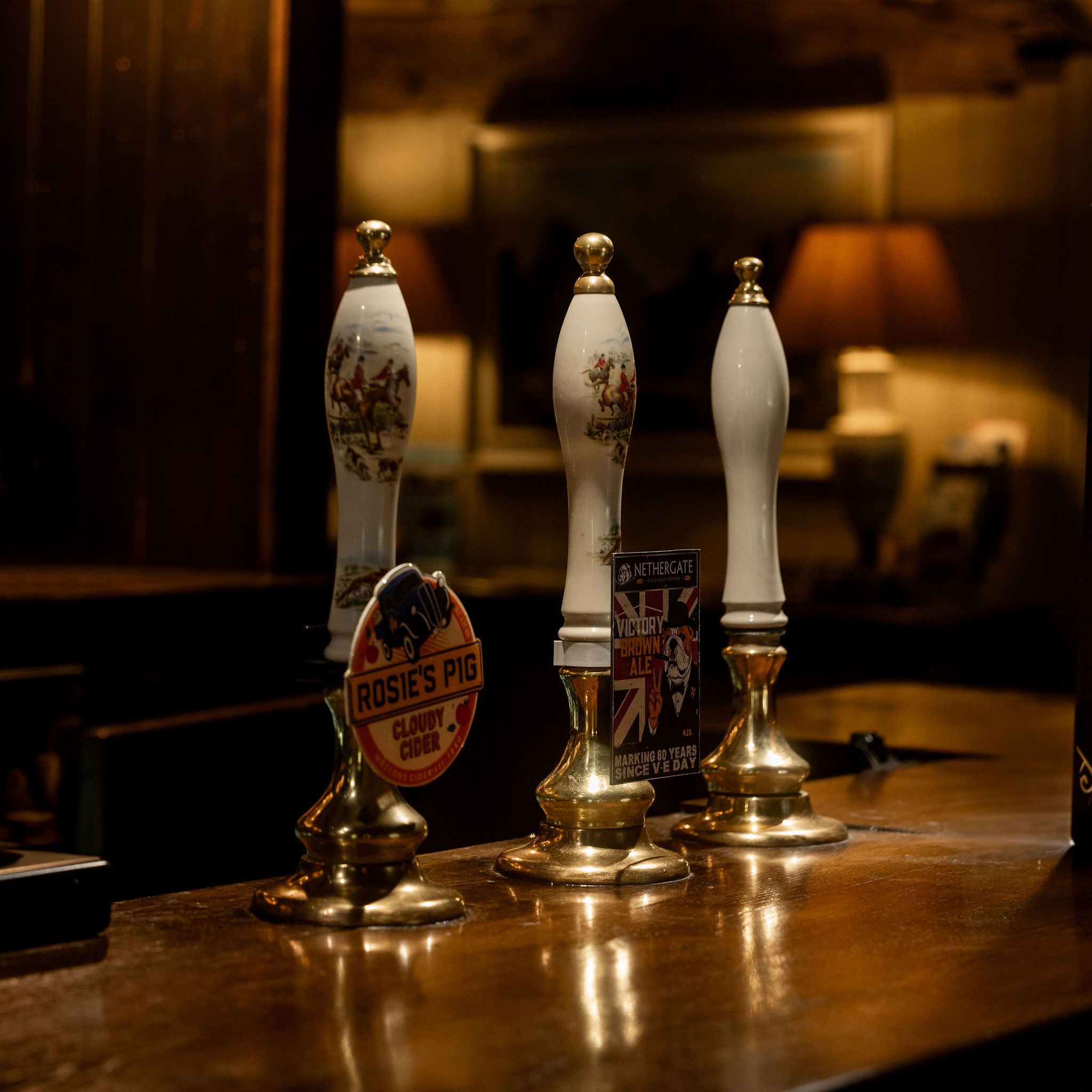 Traditional ale pump handles on a wooden bar in a dimly lit pub.