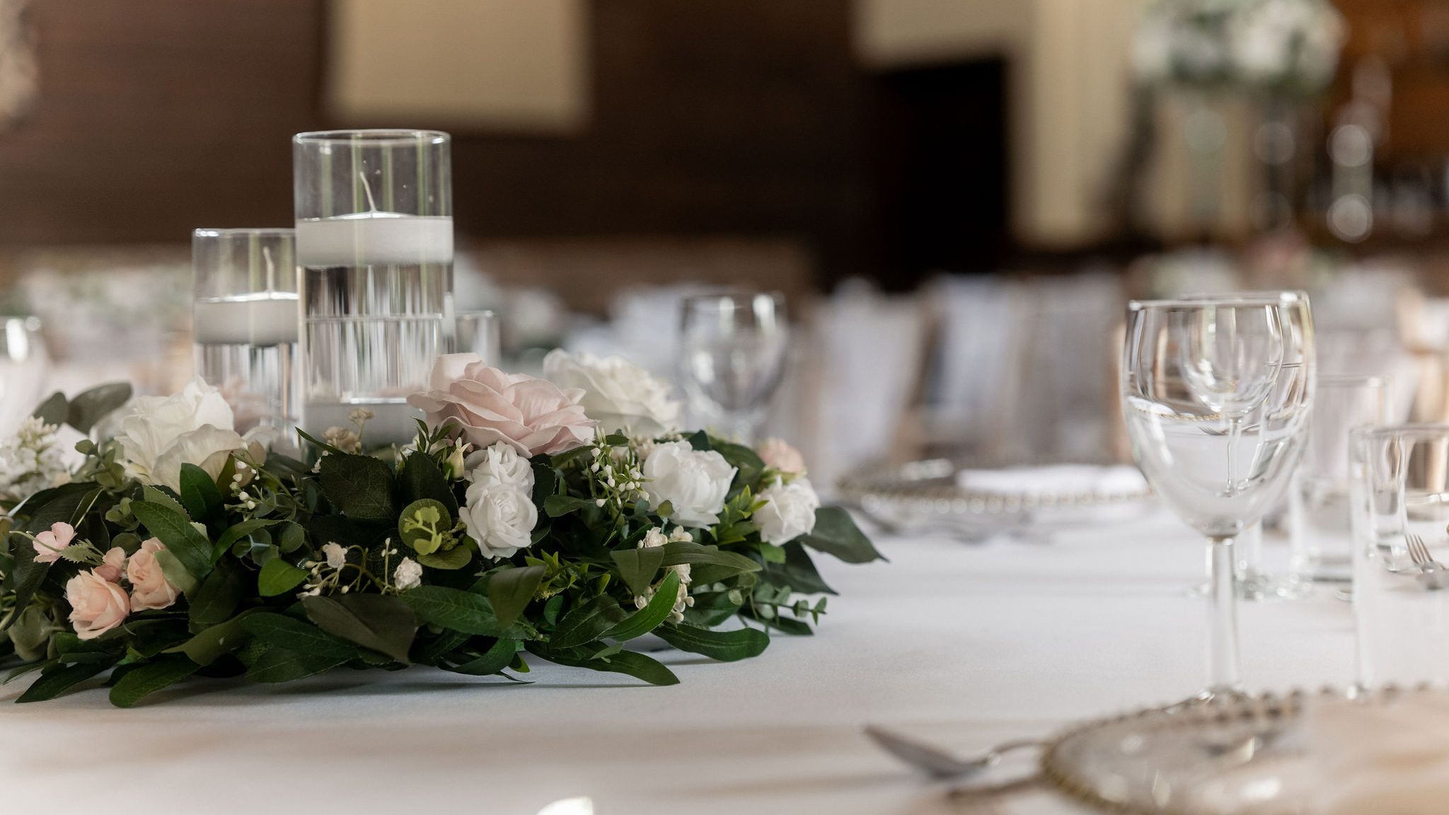 Elegant table setting with floral centerpiece, floating candles in glass holders, and empty wine glasses on a white tablecloth.