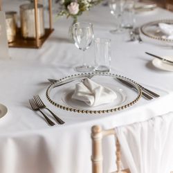 Elegant table setting with a white tablecloth, a decorative plate with a folded white napkin, silverware, glassware, and a small floral centerpiece.