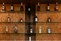 Shelves with various bottles of alcoholic beverages including wine, liqueur, and spirits displayed against a textured brown wall.