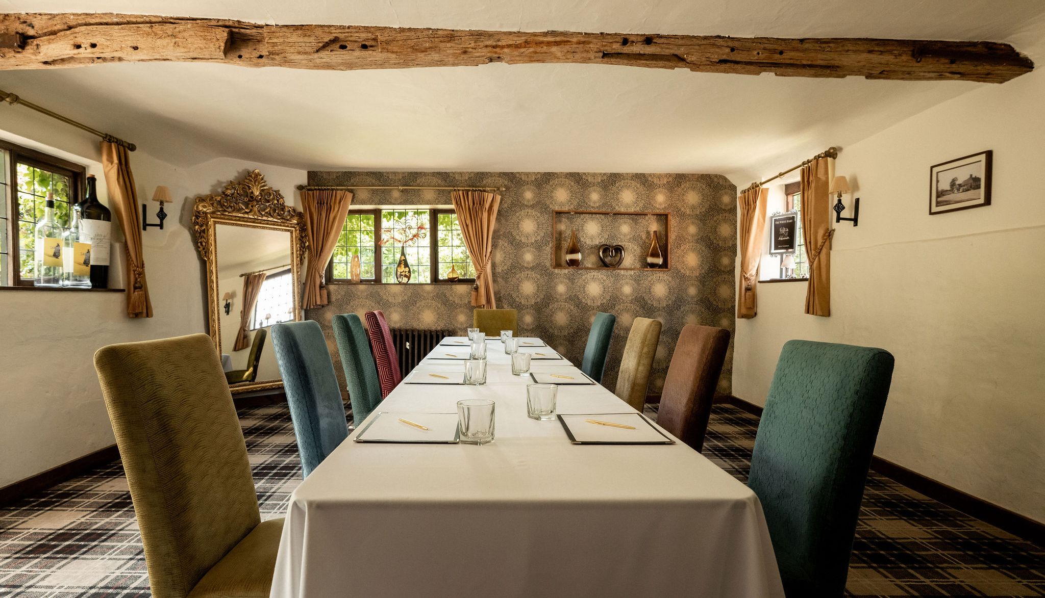 A cozy meeting or dining room with a long table, assorted colorful chairs, and rustic decor.