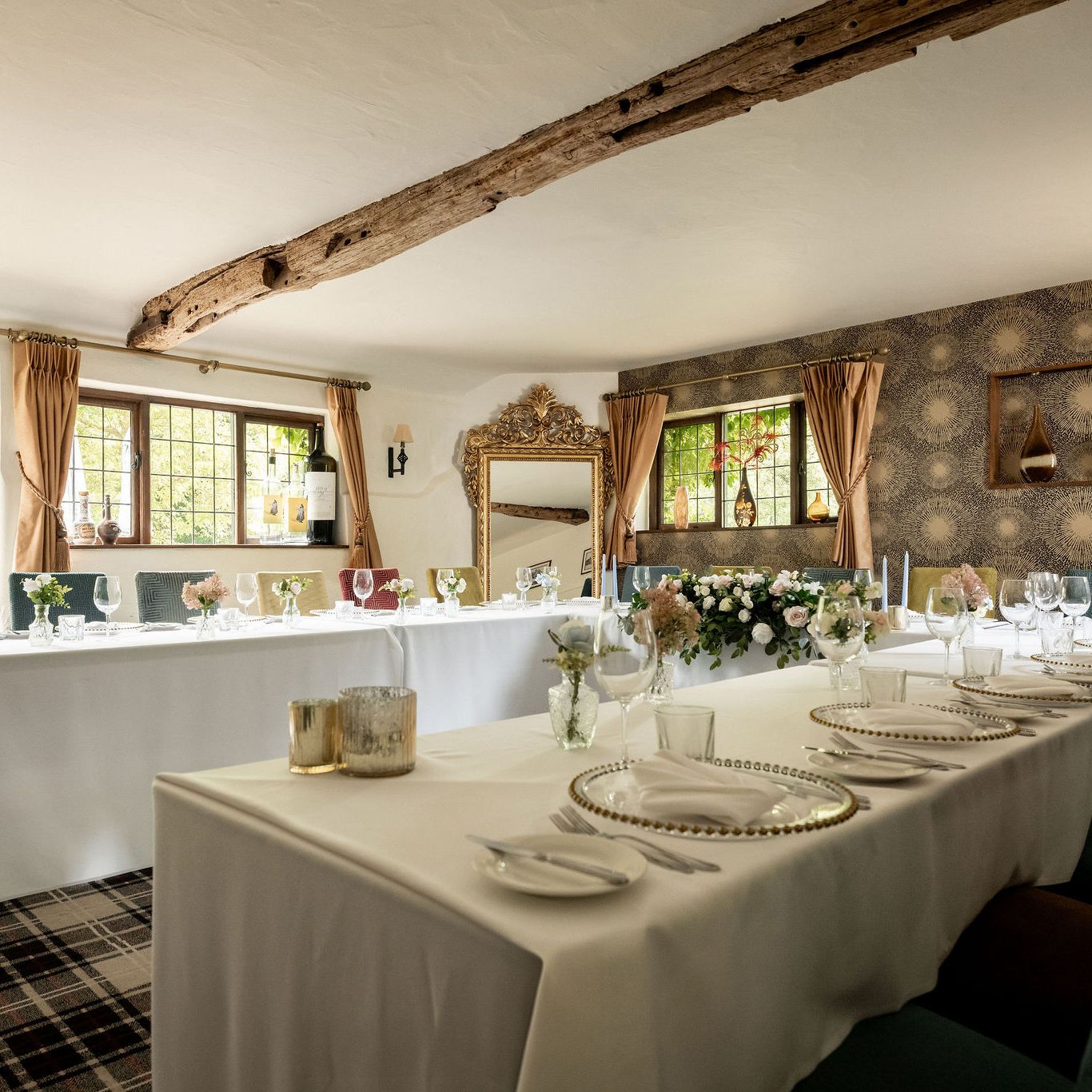 Elegant dining room setup with white tablecloths, floral centerpieces, and decorative elements in a cozy, light-filled space.