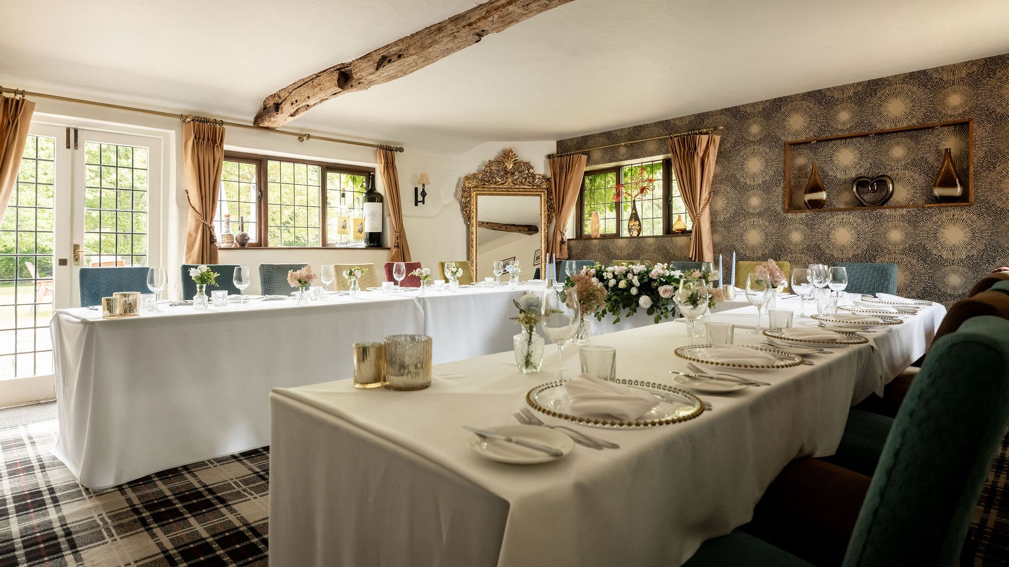 Elegant dining room setup with white tablecloths, floral centerpieces, and decorative elements in a cozy, light-filled space.