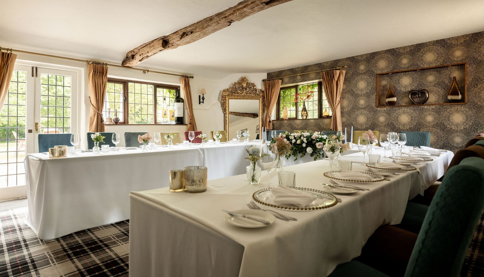 Elegant dining room setup with white tablecloths, floral centerpieces, and decorative elements in a cozy, light-filled space.