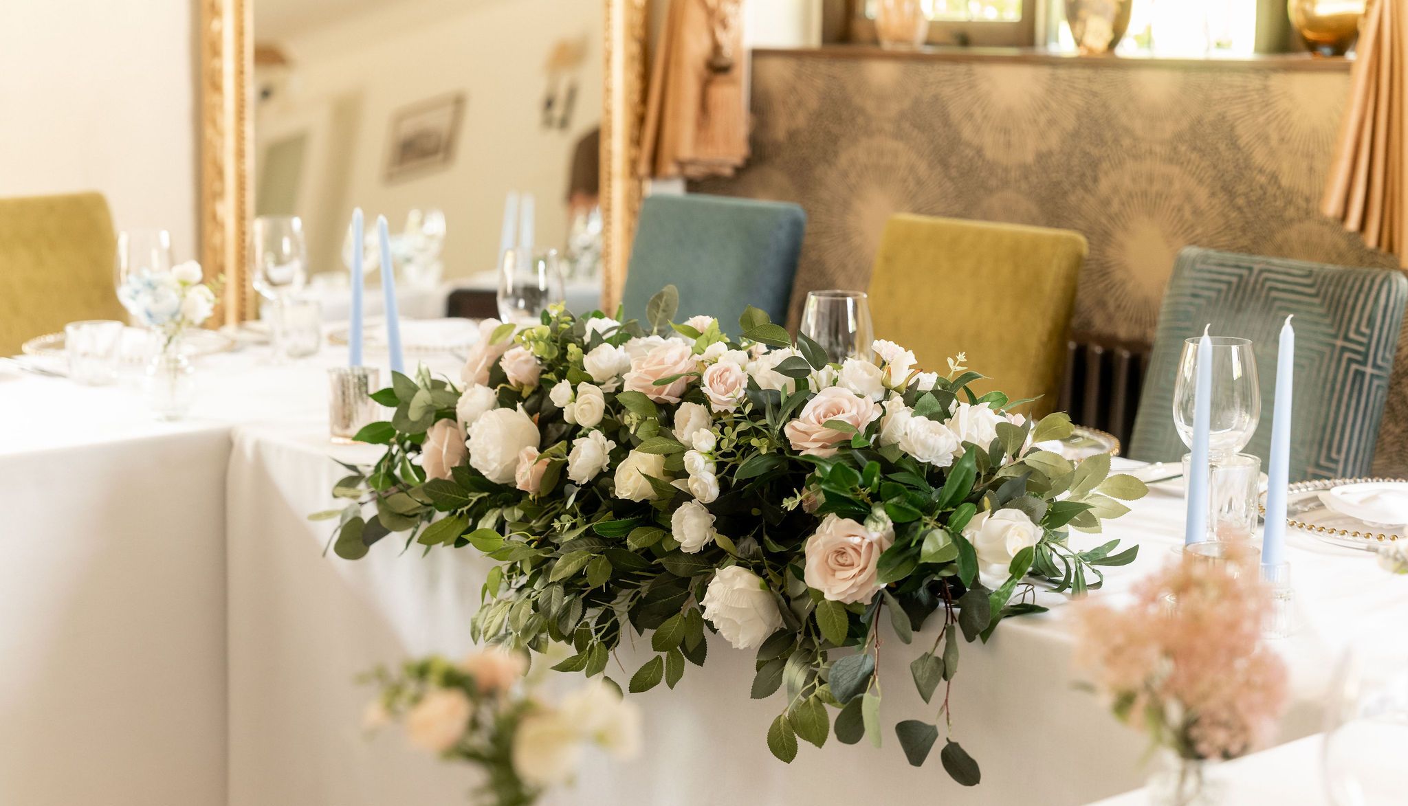 Elegant wedding table arrangement with white and blush pink flowers, greenery, and light blue candles.