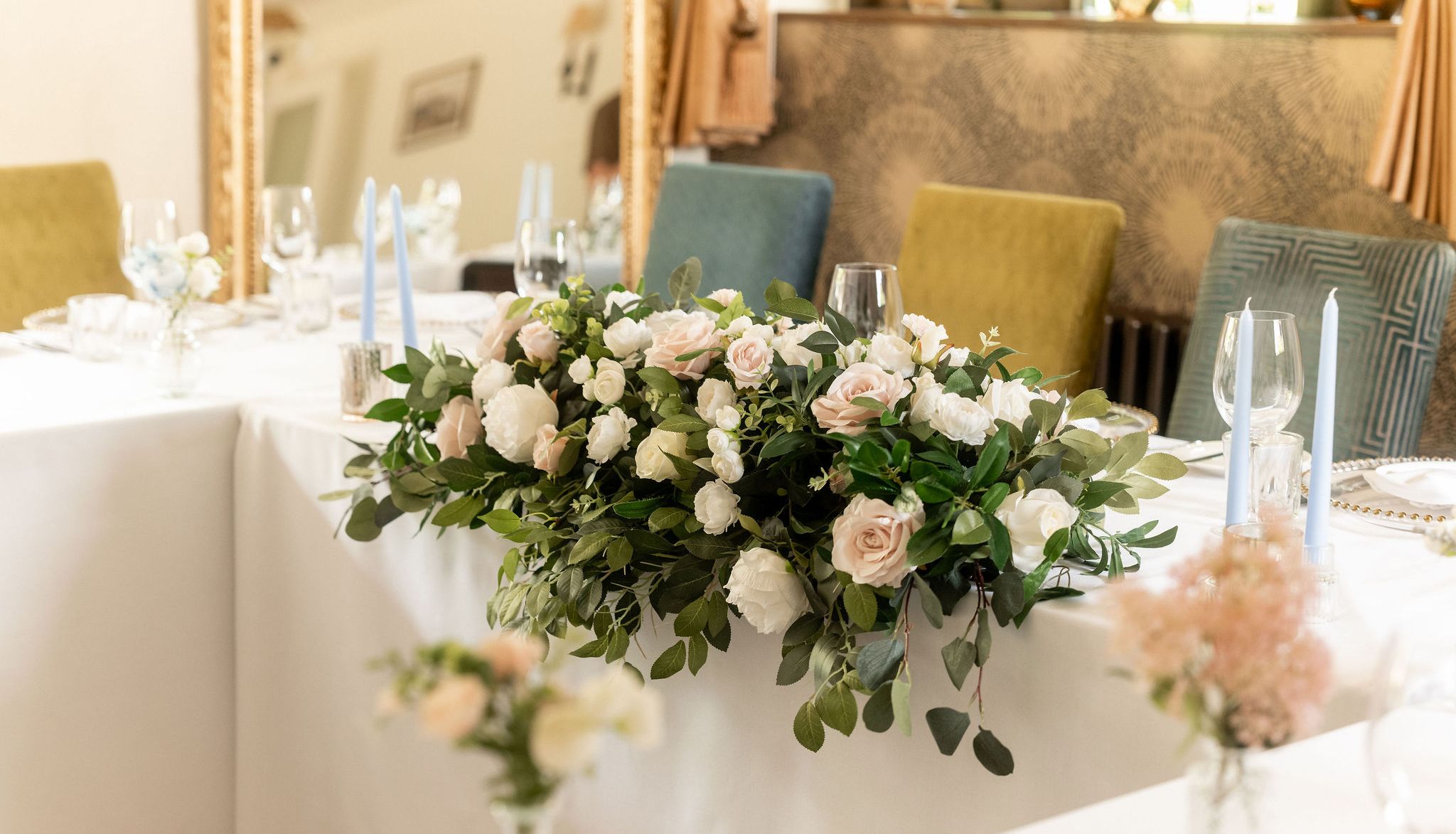 Elegant wedding table arrangement with white and blush pink flowers, greenery, and light blue candles.