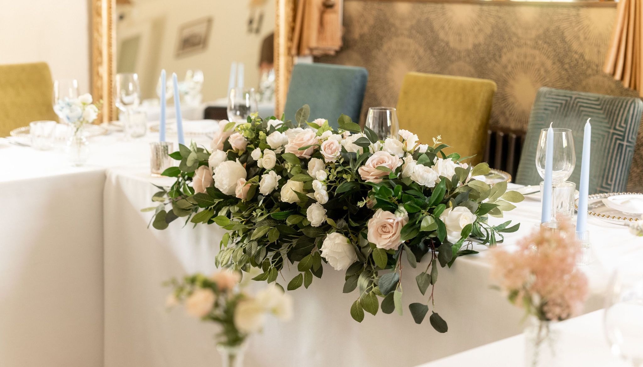 Elegant wedding table arrangement with white and blush pink flowers, greenery, and light blue candles.