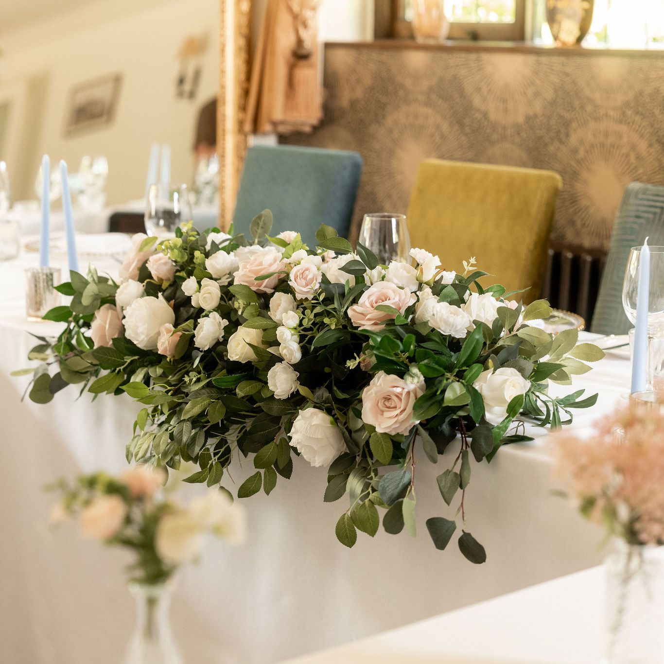 Elegant wedding table arrangement with white and blush pink flowers, greenery, and light blue candles.