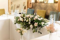 Elegant wedding table arrangement with white and blush pink flowers, greenery, and light blue candles.