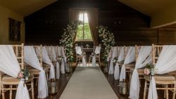 Rustic indoor wedding ceremony setup with floral arch and draped chairs