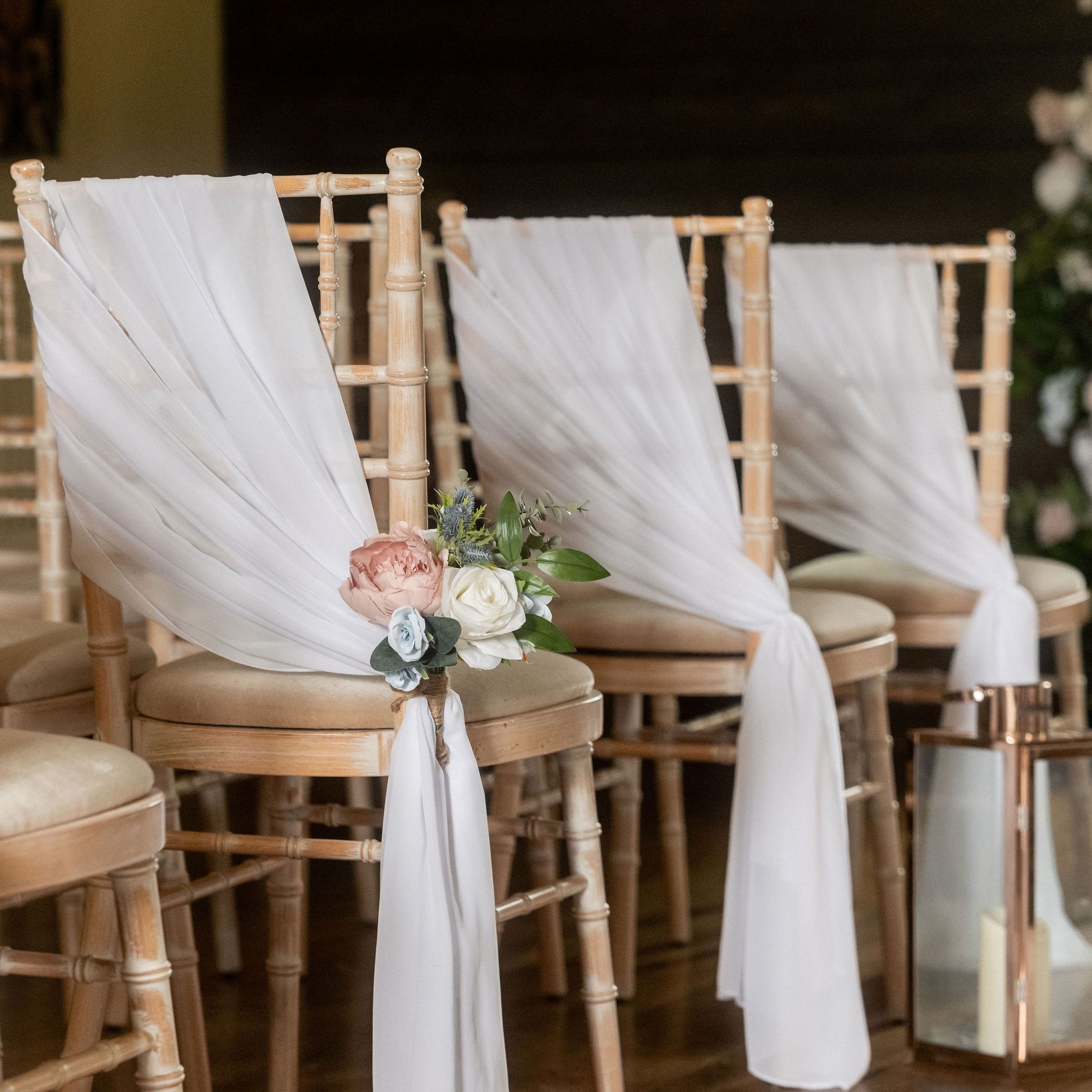 Row of wooden chairs decorated with white fabric and floral arrangements for a wedding ceremony