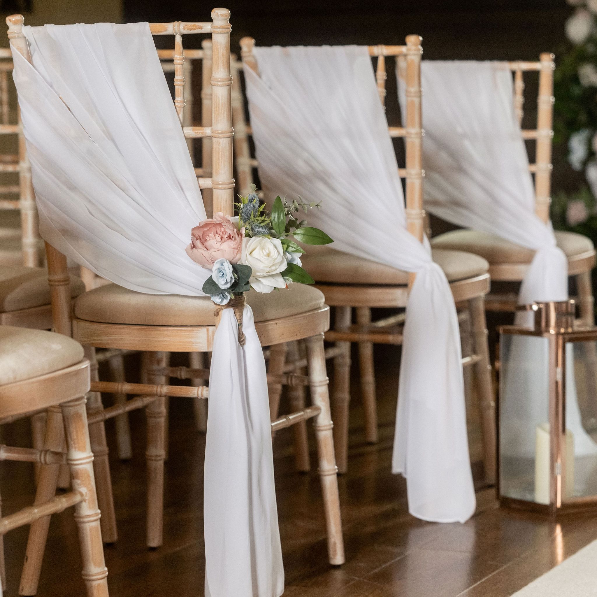 Row of wooden chairs decorated with white fabric and floral arrangements for a wedding ceremony