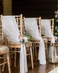 Row of wooden chairs decorated with white fabric and floral arrangements for a wedding ceremony