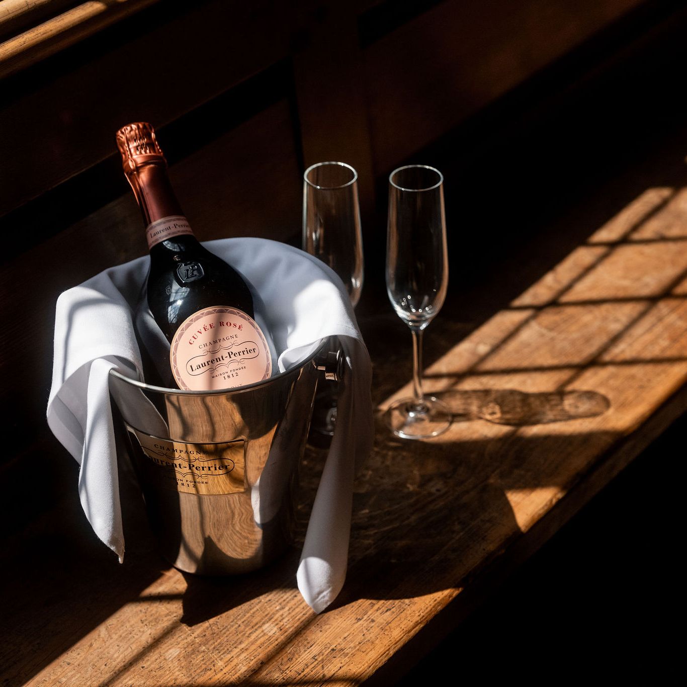 Bottle of Laurent-Perrier champagne in an ice bucket with two empty champagne flutes on wooden surface