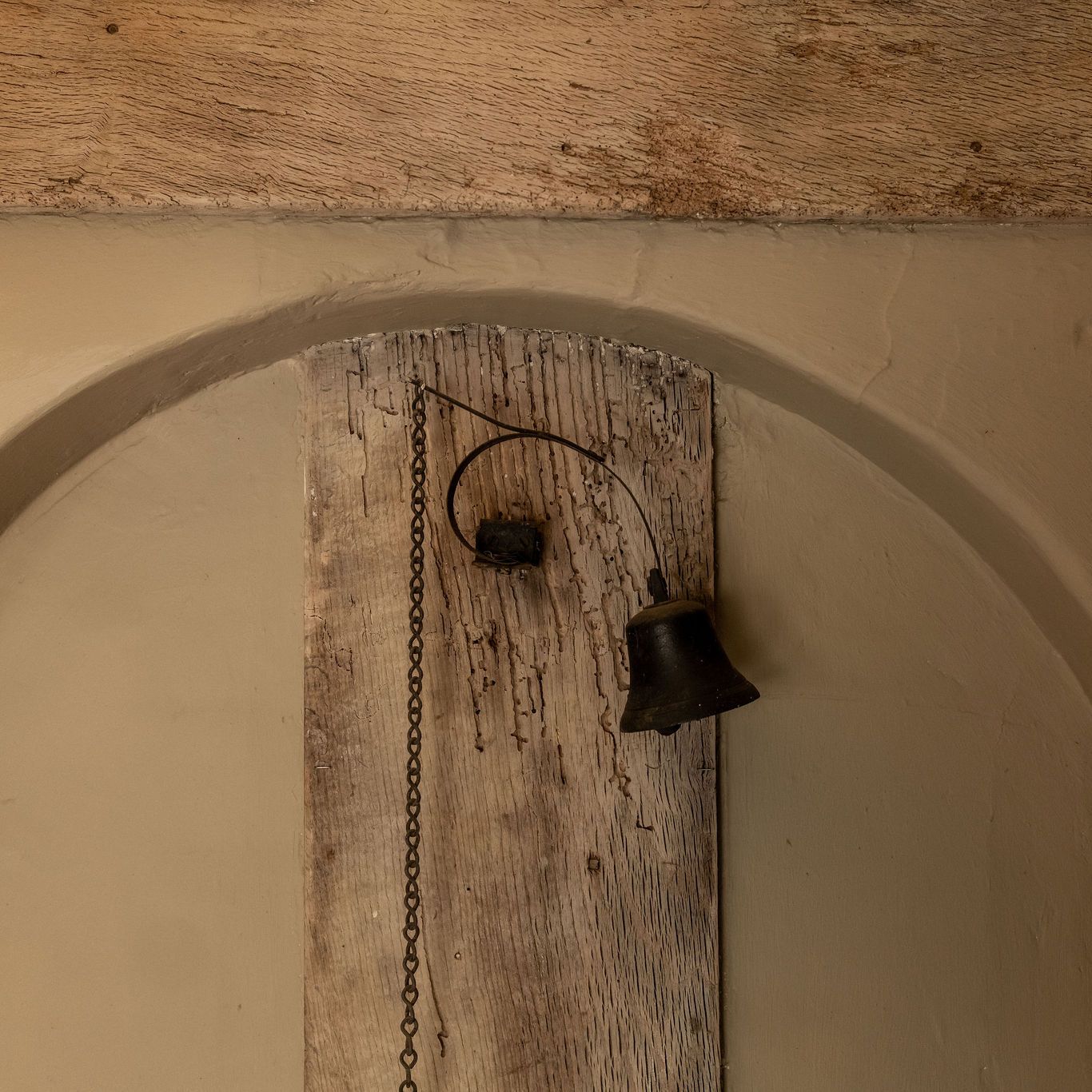 Old rustic metal bell attached to a wooden board with a hanging chain.
