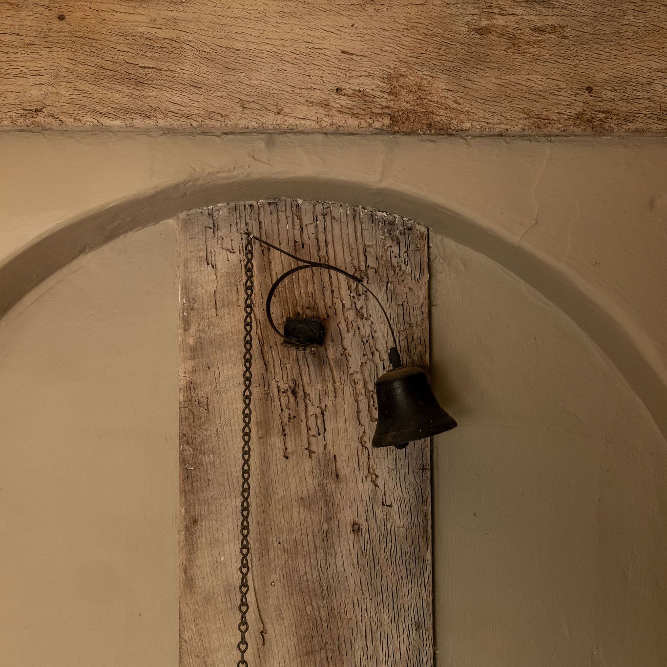 Old rustic metal bell attached to a wooden board with a hanging chain.