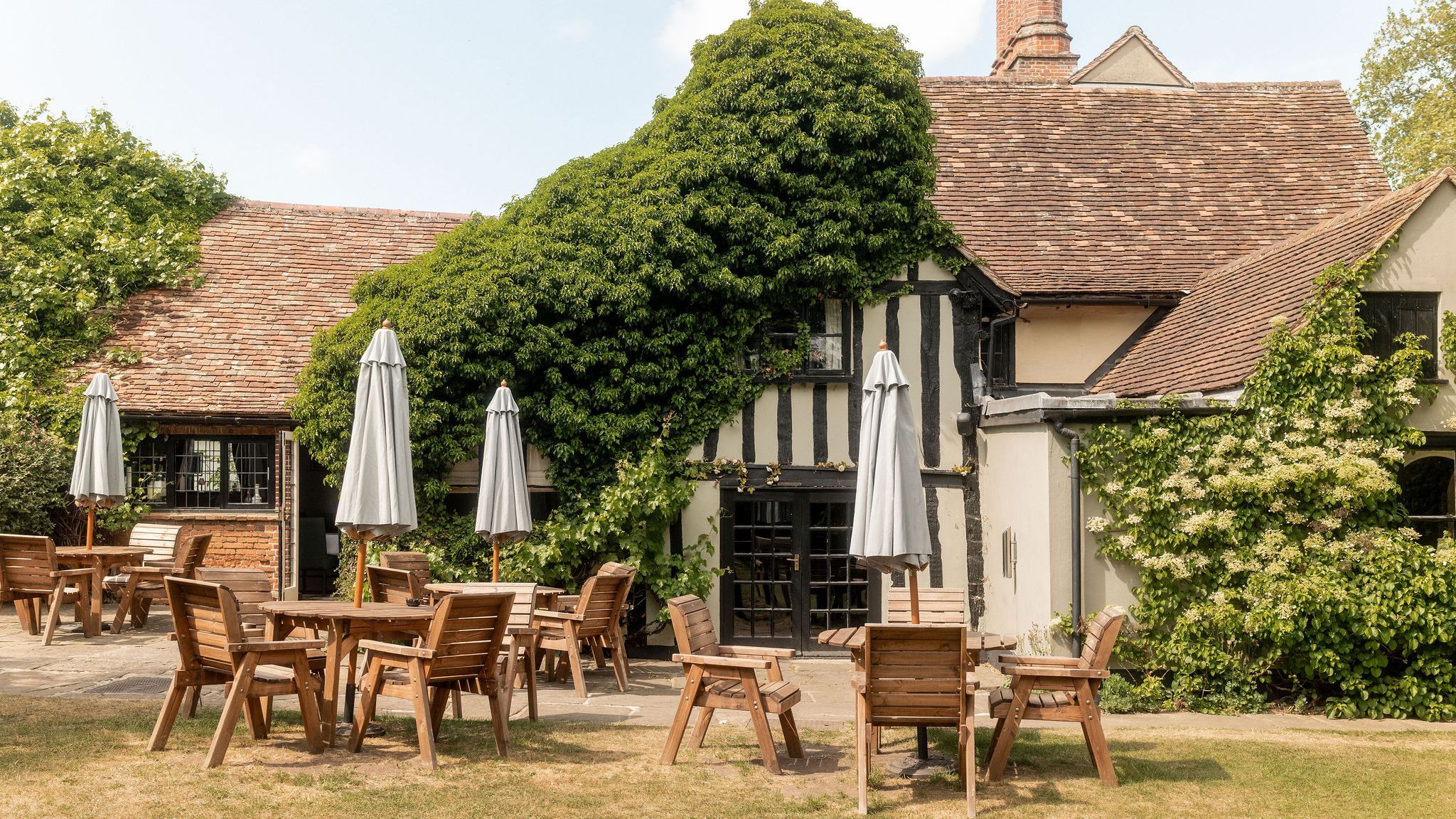 Outdoor patio with wooden tables and chairs in front of a charming, ivy-covered building