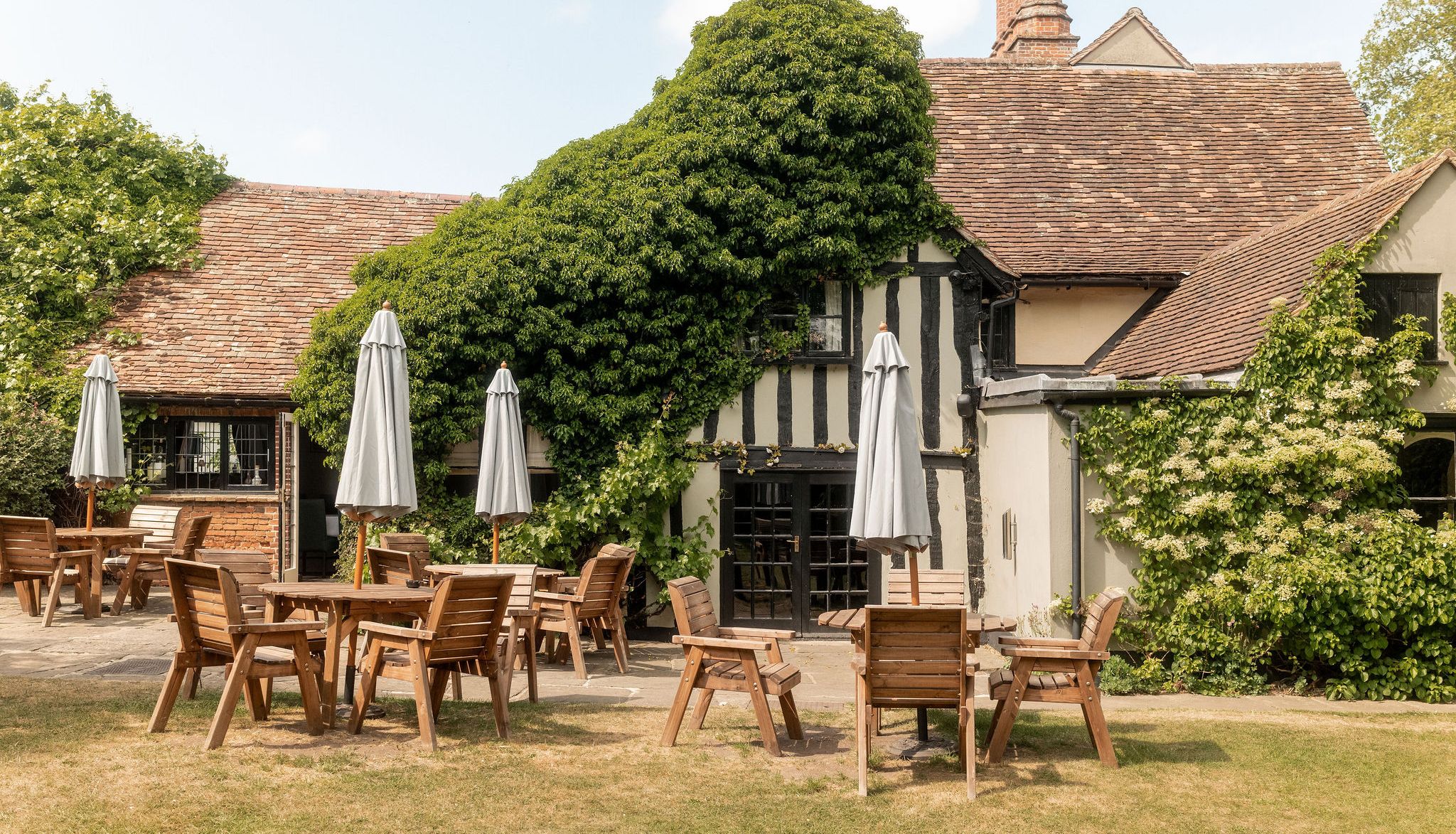 Outdoor patio with wooden tables and chairs in front of a charming, ivy-covered building