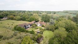 Aerial view of a countryside estate with multiple buildings and lush green gardens surrounded by fields and trees.