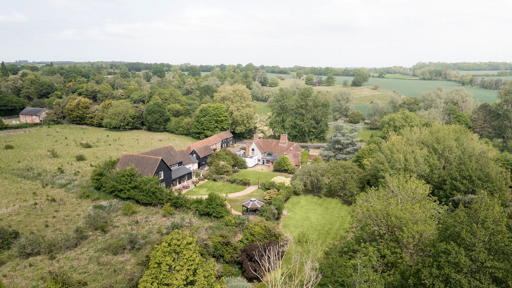Aerial view of a countryside estate with multiple buildings and lush green gardens surrounded by fields and trees.