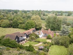 Aerial view of a countryside estate with several buildings, trees, gardens, and open green spaces.