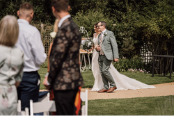 Bride and a man walking down an outdoor aisle at a wedding with guests in the foreground.