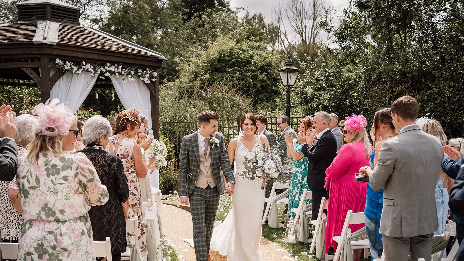 Bride and groom walking down the aisle outdoors after their wedding ceremony, surrounded by clapping guests.