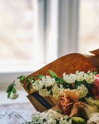 A close-up of a colorful bouquet of flowers, including pink ranunculus and white blossoms, placed on a wooden table near a window.
