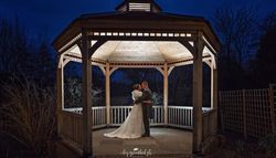 Bride and groom embrace in a beautifully lit wooden gazebo at night.