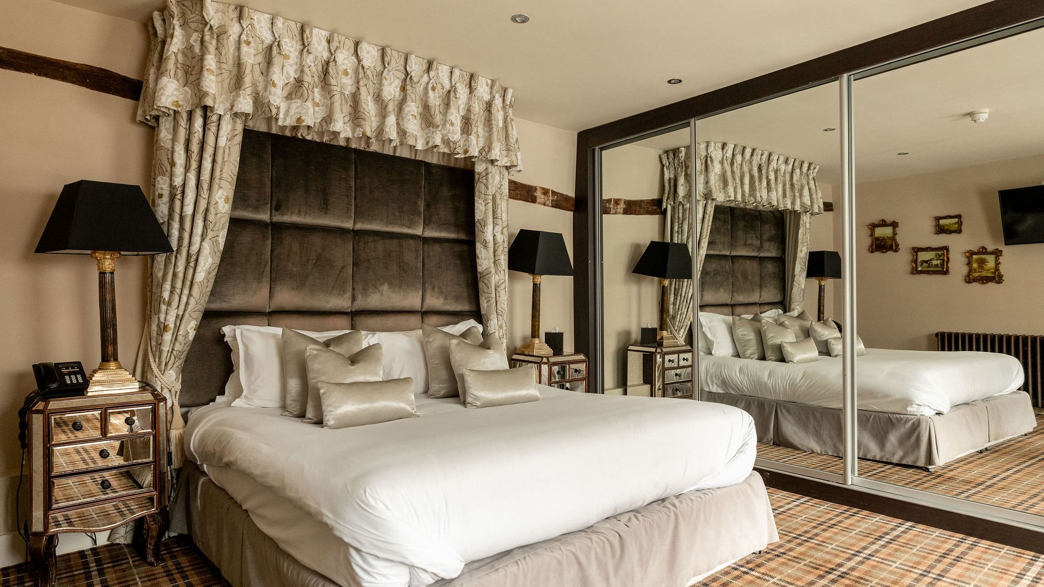 Luxurious hotel bedroom with a large bed, elegant bedding, mirrored wardrobe, patterned carpet, and stylish bedside tables with lamps.