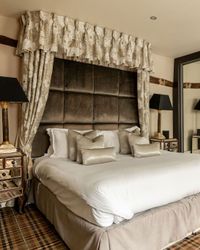 Luxurious hotel bedroom with a large bed, elegant bedding, mirrored wardrobe, patterned carpet, and stylish bedside tables with lamps.