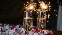 Two champagne glasses with sparklers, festive pinecone wreath and red ribbon on wooden table