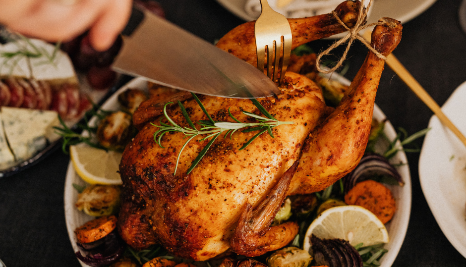 Person carving a roasted whole chicken garnished with herbs and vegetables