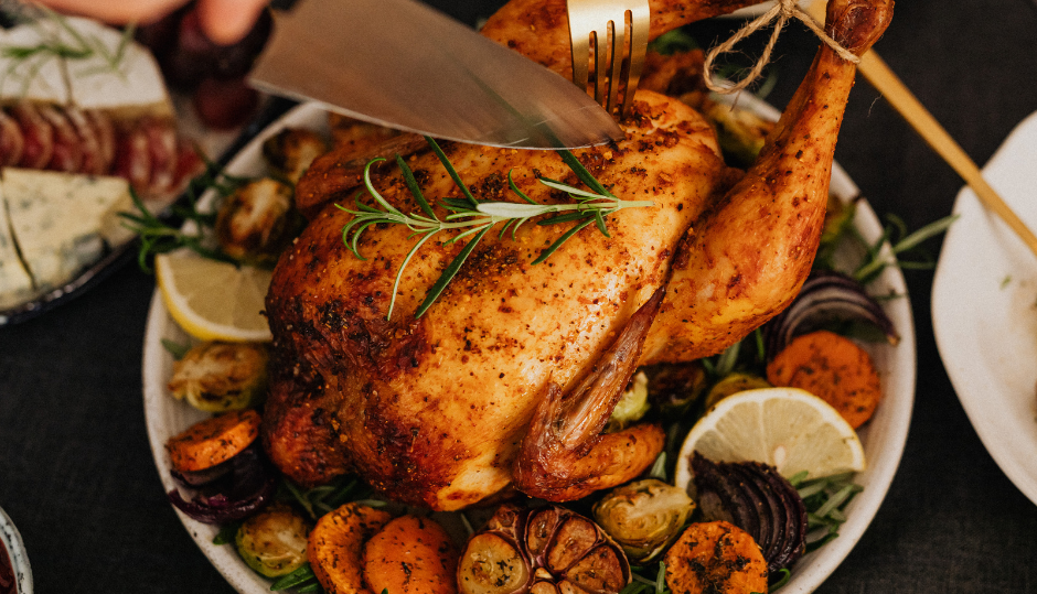 Person carving a roasted whole chicken garnished with herbs and vegetables