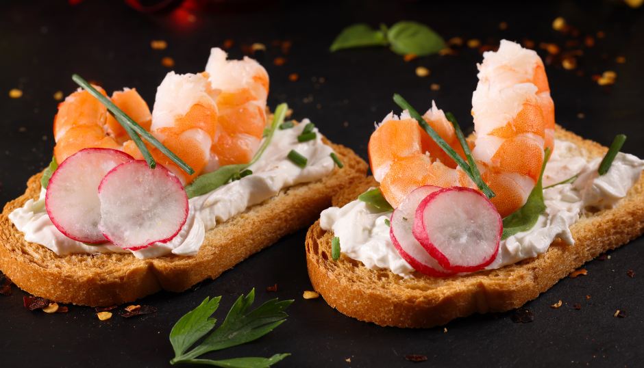 Toasted bread slices topped with cream cheese, shrimp, radish slices, and herbs.