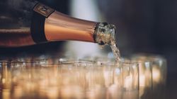 A close-up shot of a champagne bottle pouring sparkling wine into a row of clear glasses.