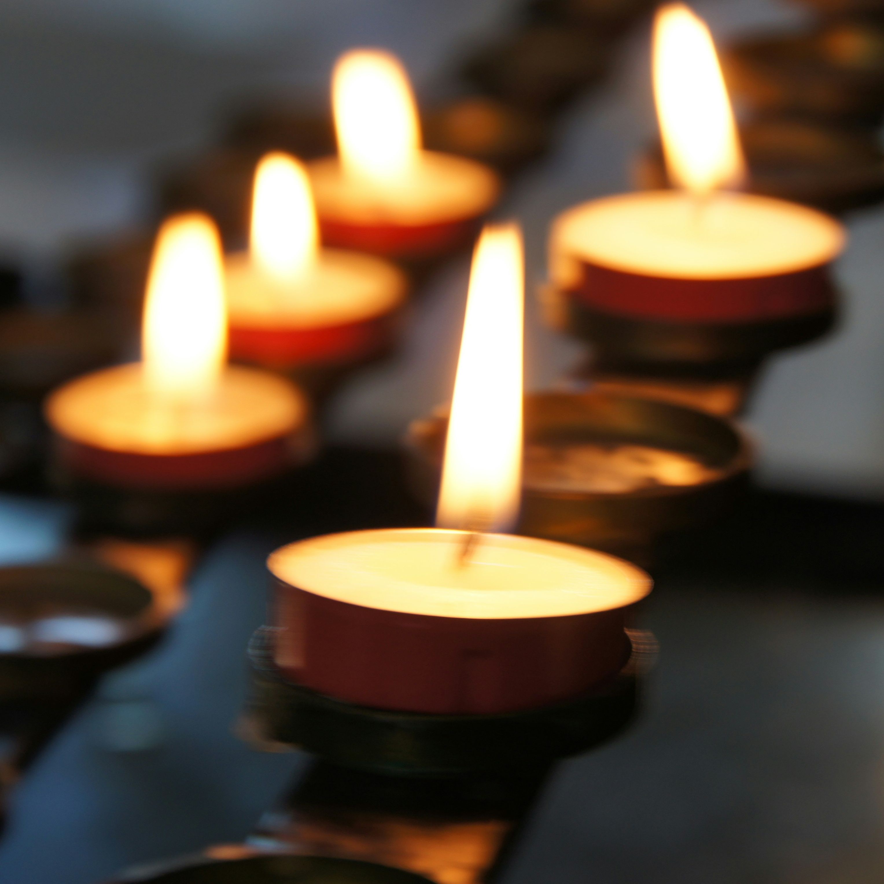 Several tealight candles burning in a row with a soft focus background