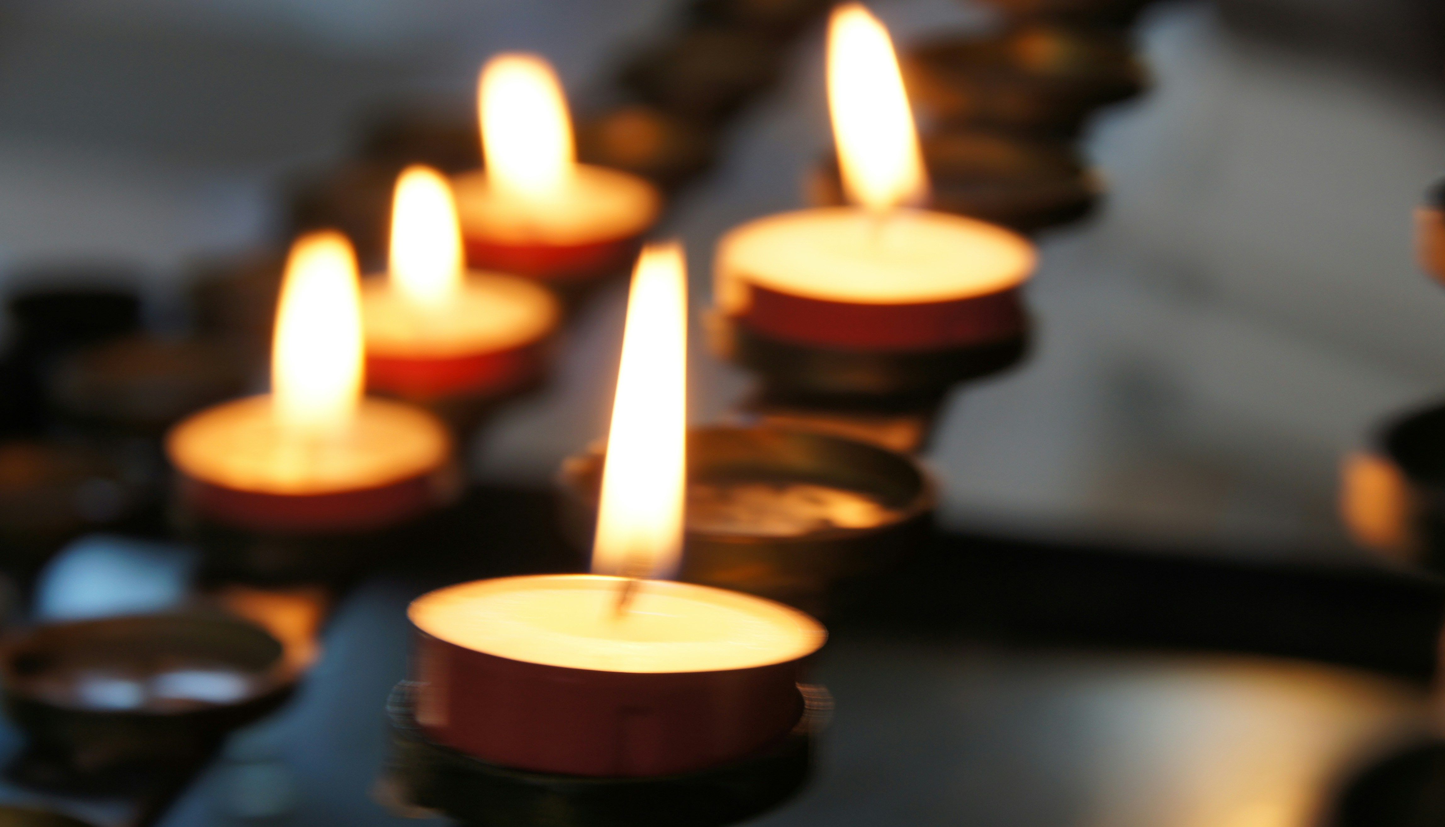 Several tealight candles burning in a row with a soft focus background
